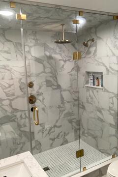 A custom walk-in shower with gray tiles and gold fixtures and a frameless glass shower door with gold hardware installed by Glass Doctor of Sarasota.